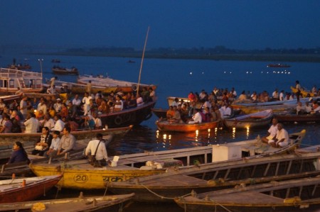 Boats full of people waiting to watch the prayer ceremony on the Ghats at night. The points of light in the water are candles floating on flowers, each representing a prayer.