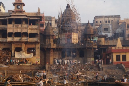 Temple along the Ganges illuminated by the sunrise, the ashes of a funeral pyre still smoking from the previous day.